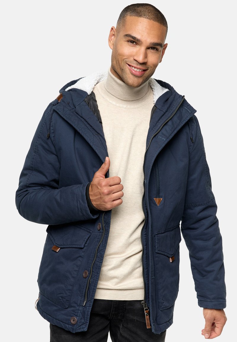 Navyblauwe geïsoleerde jas met een capuchon, voorzien van een faux fur voering, rits- en knoopsluiting, en leren accenten op de zakken.