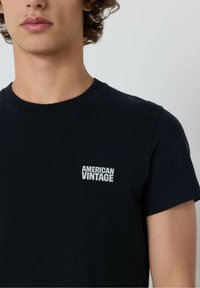 Čierne bavlnené tričko s okrúhlym výstrihom. Biele logo "AMERICAN VINTAGE" potlačené na ľavej hrudi. Krátke rukávy, základný strih. Hladká textúra.