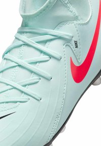 Crampon de football bleu clair avec un upper texturé, logo Nike rose contrastant et accents blancs, avec des lacets noirs et une semelle en caoutchouc moulé.