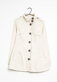 Chaqueta beige, ligera, con un cuello alto, seis botones de madera y bolsillos laterales. Cuenta con una cremallera y hombreras.