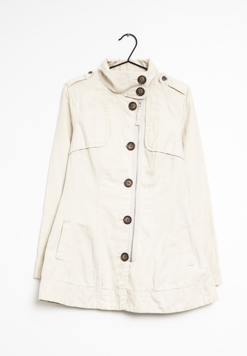 Chaqueta beige, ligera, con un cuello alto, seis botones de madera y bolsillos laterales. Cuenta con una cremallera y hombreras.