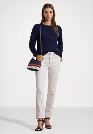 Maglione lavorato a maglia blu navy con logo in rilievo, jeans color crema e una piccola borsa a tracolla a strisce multicolori. Tacchi neri con cinturini completano il look.