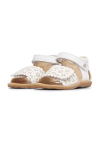Sandali bianchi in pelle con motivi floreali ritagliati, bordi scallop e cinturino regolabile. Suola in gomma tan e rivestimento interno morbido.
