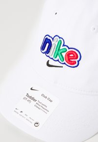 Balta medvilninė kepuraitė su daugiakampiu siuvinėtu "nike" logotipu, su juodu swoosh; apima etiketę, nurodančią mažylio dydį (2T-4T).
