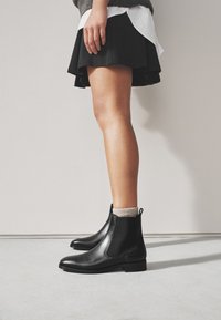 Zwarte leren Chelsea-laarzen met elastische zijpanelen en een treklus, met een strak ontwerp en een lage blokhak.
