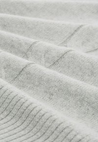 Helles graues Gewebe mit einer weichen Textur, das ein geripptes Muster und glatte Abschnitte aufweist, die in sanften Falten angeordnet sind und einen geschichteten Eindruck erzeugen.