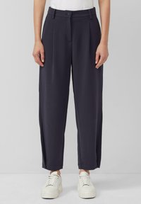Marineblauwe wijde broek met hoge taille, geplooide voorkant en zijzakken, gecombineerd met witte sneakers voor een casual look.