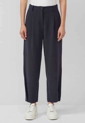 Pantalons larges de couleur marine avec une taille haute, un devant plissé et des poches latérales, associés à des baskets blanches pour un look décontracté.