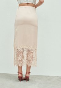 Ołowiankowa spódnica z miękkiego różowego materiału z koronkowym obszyciem zdobionym kwiatowym wzorem. Boczne rozcięcie, w duecie z różowymi sandałkami na paski.