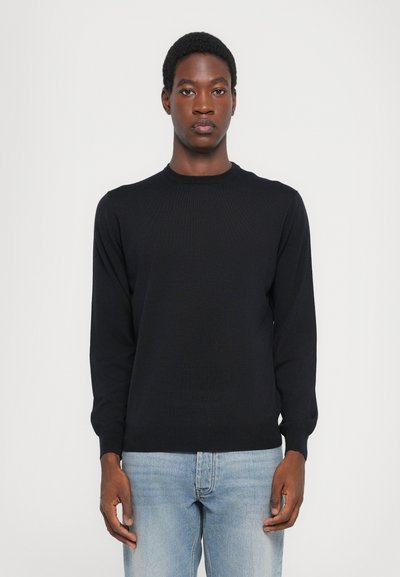 Zwarte langarmtrui met ronde hals, gemaakt van gebreide stof, gedragen over lichtblauwe jeans, met een slim fit en ribgebreide manchetten.