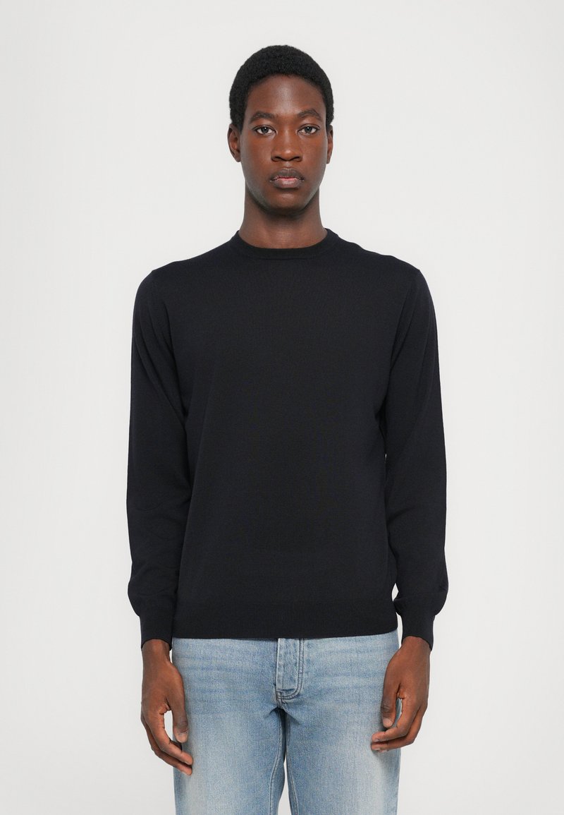 Black long-sleeve sweater with a crew neck, made of knitted fabric, worn over light blue jeans, featuring a slim fit and ribbed cuffs.