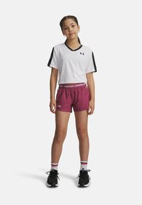 Witte cropped sporttop met zwarte mouwen, gecombineerd met bordeauxkleurige shorts met een elastische tailleband. Zwarte sportschoenen met witte accenten.