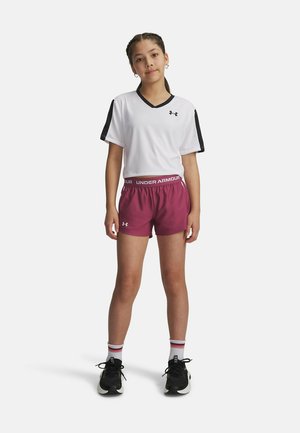 Vit cropped sportstopp med svarta ärmar, kombinerad med vinröda shorts med resårmidja. Svarta träningsskor med vita detaljer.
