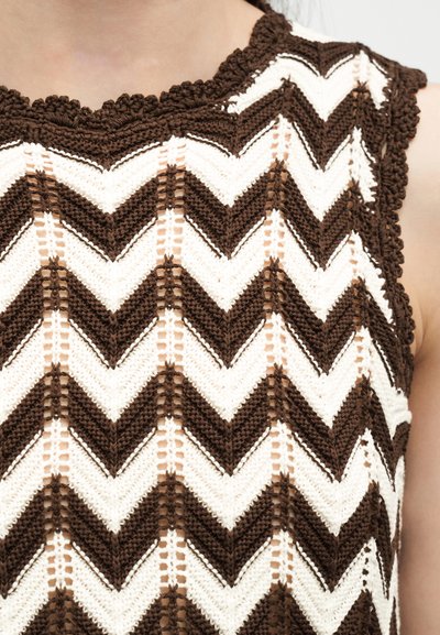 Αμάνικη πλεκτή μπλούζα με καφέ και λευκό σχέδιο ζιγκ-ζαγκ και κυματιστά τελειώματα, φορεμένη πάνω σε γυμνό δέρμα.