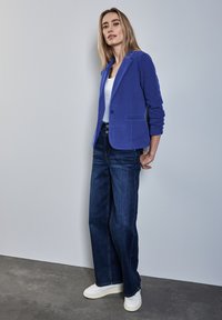 Blå, skräddarsydd blazer av mjukt tyg, kombinerad med högmidjade, vida mörk denimjeans och vita sneakers. Enkelt mönster med fickor.