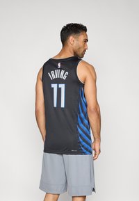 Schwarzes Basketballtrikot mit blauen Seitenstreifen, auf der Rückseite "IRVING" und die Nummer "11", aus atmungsaktivem Mesh-Gewebe. Graue Shorts sichtbar.