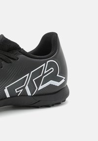 Zapatilla deportiva negra con parte superior texturizada, que presenta un logotipo gráfico blanco y cordones. Suela diseñada para ofrecer tracción en superficies de césped.