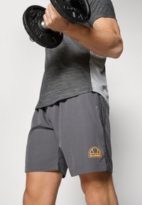 Gray athletic shorts with an orange logo, paired with a gray and black striped short-sleeve shirt, while holding a black dumbbell.