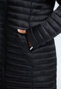 Schwarze Pufferjacke mit horizontaler Steppstruktur, ausgestattet mit einem Reißverschluss und Seitentaschen. Die Ärmel haben einen leicht gerippten Abschluss.