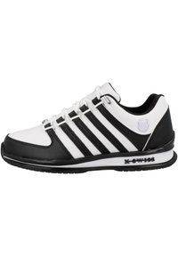Weiße Sportschuhe mit schwarzen Akzenten, ausgestattet mit einem glatten Lederobermaterial, drei schwarzen Streifen, einer gepolsterten Sohle und metallischen Ösen.