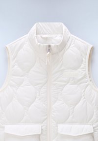 Chaleco blanco acolchado sin mangas con cuello alto, cremallera frontal, dos bolsillos delanteros con solapa y sutil logo en relieve en el pecho.