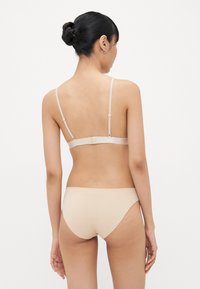 Beige beha en bijpassende slipset met verstelbare bandjes, gladde textuur en eenvoudig design. Achteraan zicht toont de haaksluiting op de beha.