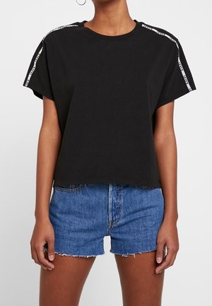 Zwart katoenen T-shirt met korte mouwen en een ronde halslijn, met witte merkranden op de schoudernaden. Draagt met blauwe denim shorts.