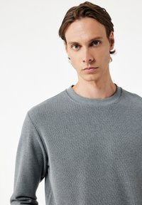 Suéter gris con canalé y cuello redondo, hecho de una tela texturizada, que presenta mangas largas y una silueta ajustada.