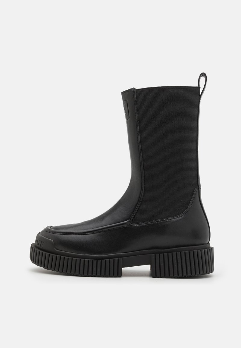 Sorte ankelstøvler med en glatt lær tå og ribbet gummisåle. Har en stretchstoffskaft og en løfteløkke bak.