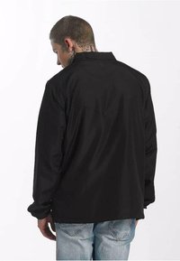 Czarna, długosleeve'owa koszula z kołnierzykiem, gładka tekstura i luźny krój, noszona na jasnoniebieskich dżinsach.