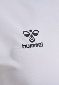 Vit polyester skjorta med en svart Hummel-logotyp, inklusive en stiliserad bi-design och ordet "hummel" i fet stil.