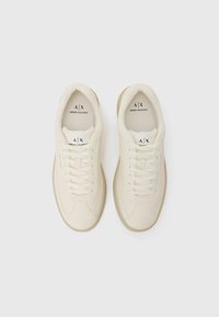 Witte leren sneakers met beige rubberen zolen en veters. Kenmerkt zich door een logo op de tong en zijkant, met een gladde en gestructureerde oppervlakte.