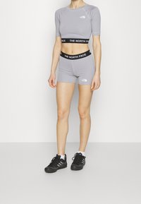 Persona que lleva un top corto de color púrpura claro y pantalones cortos a juego, con cinturillas negras de la marca "The North Face" y zapatillas negras.