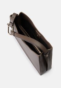 Καφέ δερμάτινη τσάντα χειρός με λεία υφή, ανοιχτό πάνω μέρος, ρυθμιζόμενο λουρί και χρυσές λεπτομέρειες. Το εσωτερικό διαθέτει πολλαπλές θήκες.