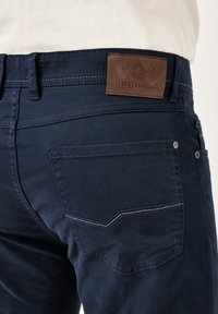 Dark blue cotton pants featuring a leather patch labeled "redpoint," with visible stitching and a back pocket detail.