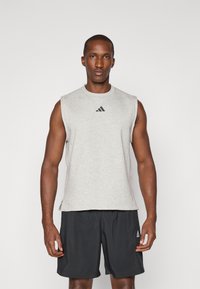 T-shirt de sport sans manches gris avec un col rond et le logo Adidas noir, associé à un short noir. Tissu lisse avec une coupe décontractée.