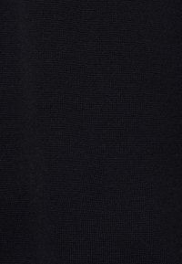 La texture du tissu noir présente un motif de tricot avec une surface douce et légèrement côtelée. Le matériau semble dense et de couleur uniforme.