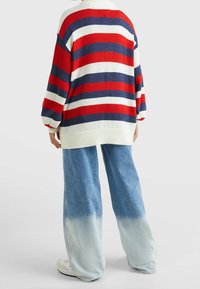 Gestreifter Pullover in Rot, Weiß und Marineblau; großzügige Passform und gerippte Bündchen. Kombiniert mit hellblauen, weit geschnittenen Jeans mit Farbverlauf.