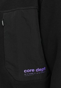 Black fleece jacket with a contrasting black, textured pocket featuring a purple logo and coordinates printed on it. Zipper detail included.