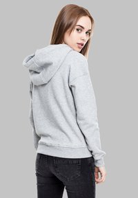 Sweat à capuche gris avec un cordon de serrage et des poignets côtelés, fabriqué en tissu doux, associé à un jean en denim foncé. Design minimaliste.