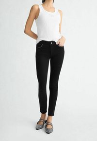 Camiseta de tirantes blanca con acanalado, jeans ajustados negros con costuras plateadas y zapatos planos negros con adornos. Diseño simple, silueta entallada.