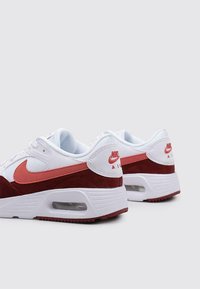 Nike Air Max Sneakers mit einem Obermaterial aus weißem Leder, burgunderroten Wildlederakzenten und einem rosa Swoosh. Verfügt über sichtbare Luftpolsterung und eine strukturiere Sohle.