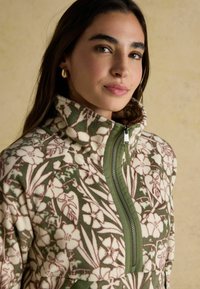 Fleecová bunda s květinovým vzorem v zelené a růžové barvě, vysokým límcem, polo-zip designem a jemnou texturou. Odolná tkanina s detaily.