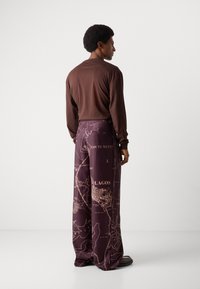 Top marrón de manga larga combinado con pantalones morados que presentan un estampado de mapa de Lagos, mostrando contornos detallados y acentos de texto.