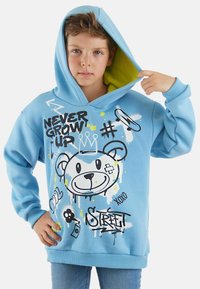 Sudadera azul clara con forro amarillo, que presenta gráficos de estilo graffiti coloridos, incluyendo la cara de un oso y el texto "NUNCA CREZCAS" en el frente.
