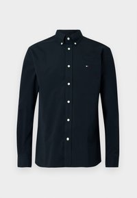 Chemise à manches longues bleu marine foncé avec col boutonné, dotée de boutons blancs et d'un petit logo tricolore sur la poitrine gauche. Tissu en coton.