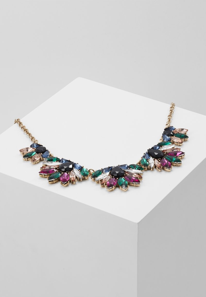Collier chaîne en or avec des grappes de pierres précieuses multicolores en noir, bleu, vert, rose et transparent sur un socle blanc d'exposition.