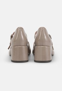 Chaussures à talons en cuir verni beige avec un bout arrondi et un talon bloc, dotées d'un détail de boucle sur le côté et de textures lisses.