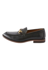 Mocassin en cuir noir à texture lisse, avec un bout légèrement arrondi et un détail en métal doré à l'avant. Accent de semelle marron.
