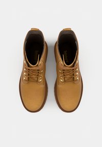 Botas de tobillo de cuero marrón con ojales dorados, cordones redondos y suela de goma. El interior tiene un forro de marca.